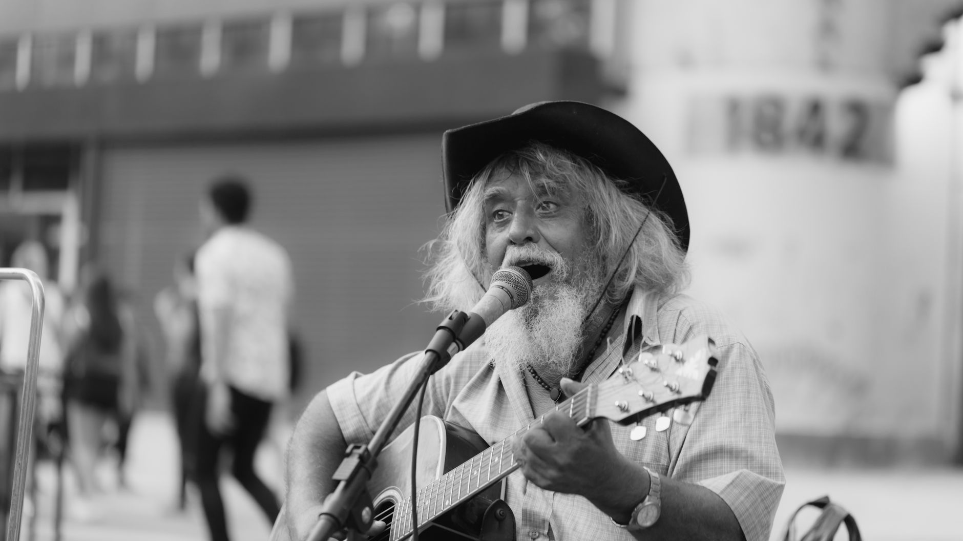 Czarno-białe zdjęcie starszego ulicznego muzyka śpiewającego z gitarą