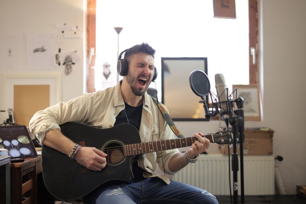 Muzyk śpiewa i gra na gitarze akustycznej w domowym studiu Muzyk śpiewa i gra na gitarze akustycznej w domowym studiu