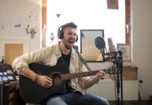 Muzyk śpiewa i gra na gitarze akustycznej w domowym studiu