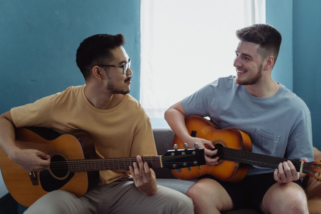 Dwóch mężczyzn gra razem na gitarach akustycznych w jasnym salonie Dwóch mężczyzn gra razem na gitarach akustycznych w jasnym salonie