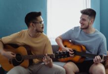 Dwóch mężczyzn gra razem na gitarach akustycznych w jasnym salonie