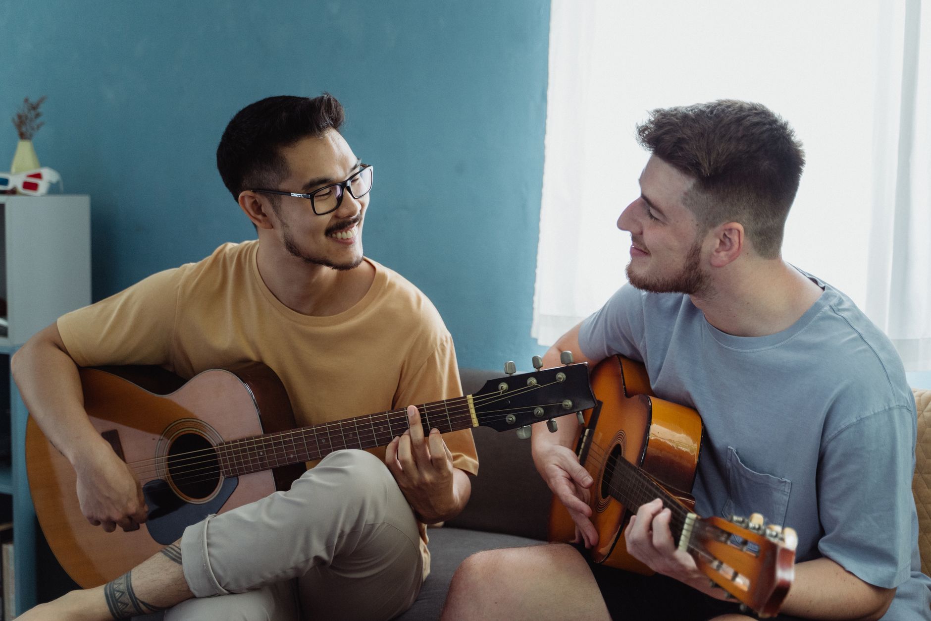 Dwóch młodych mężczyzn gra na gitarach i uśmiecha się w salonie