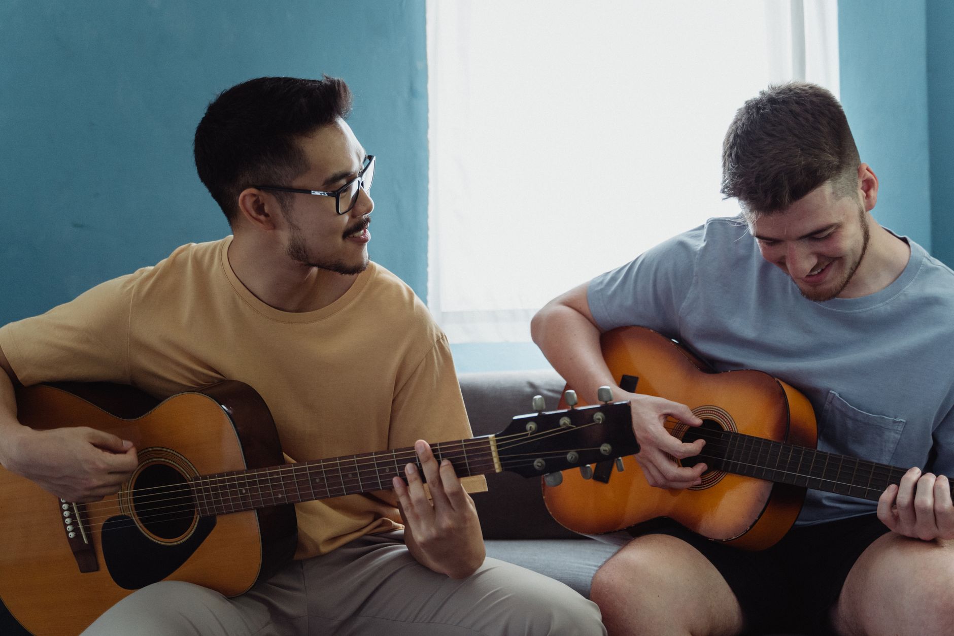 Dwóch młodych mężczyzn gra razem na gitarach akustycznych w domu
