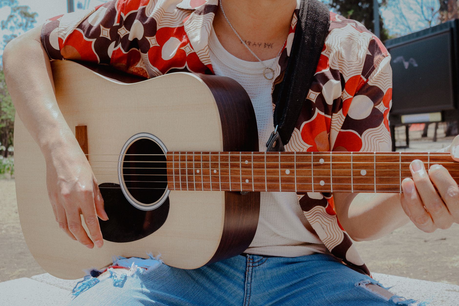 Osoba gra na gitarze akustycznej na zewnątrz w słońcu