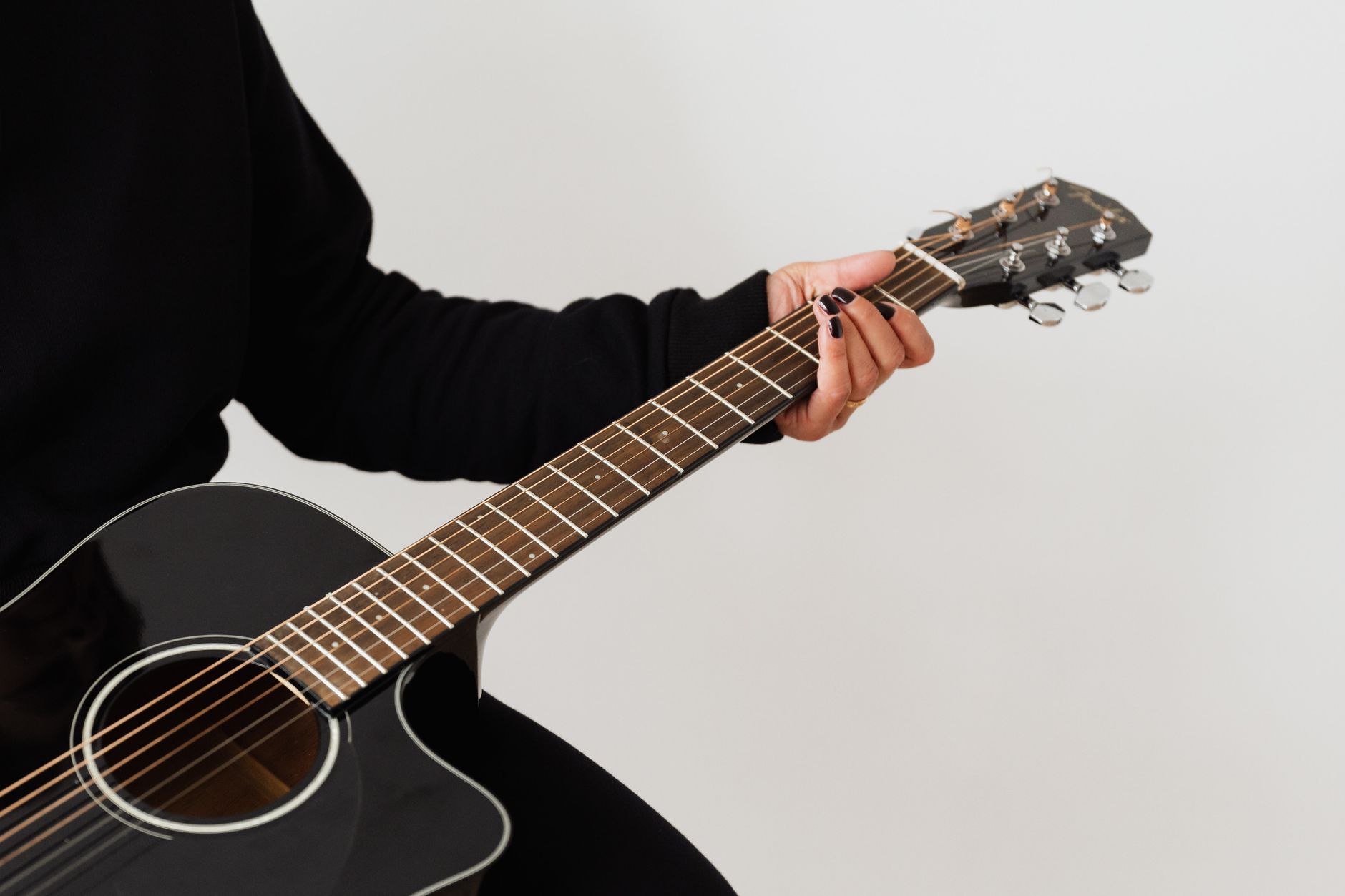 Zbliżenie dłoni trzymającej czarną gitarę akustyczną z widocznymi strunami