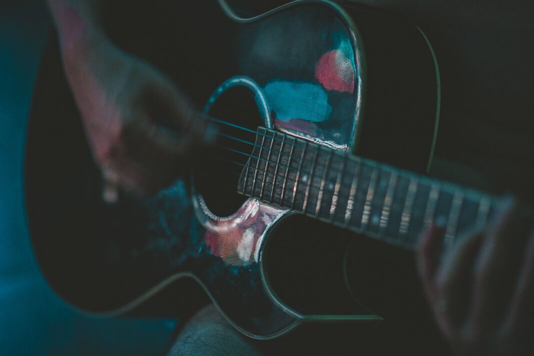 Zbliżenie muzyka grającego na akustycznej gitarze w nastrojowym świetle