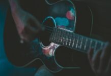Zbliżenie muzyka grającego na akustycznej gitarze w nastrojowym świetle